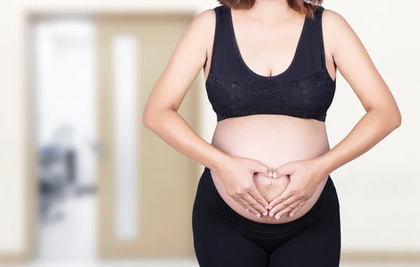 Donna incinta che tiene le mani a forma di cuore sulla pancia i — Foto Stock