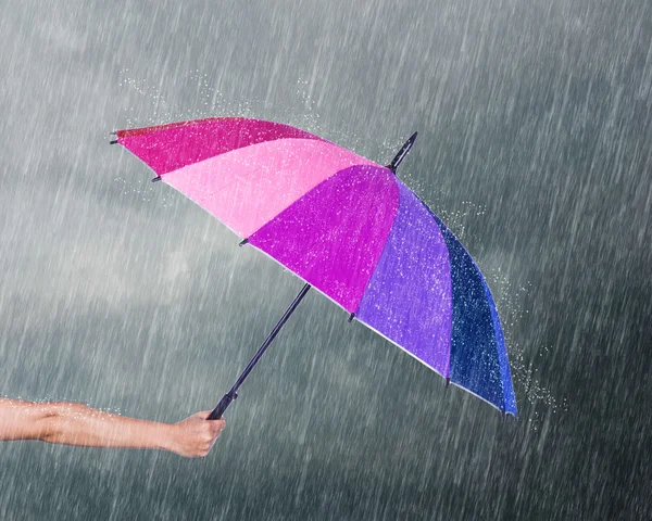 Mano sosteniendo paraguas multicolor bajo el cielo oscuro con lluvia — Foto de Stock