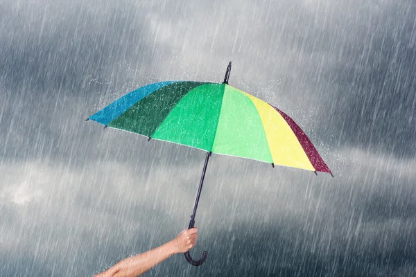 Hand som håller mångfärgad paraply under mörka himmel med regn — Stockfoto