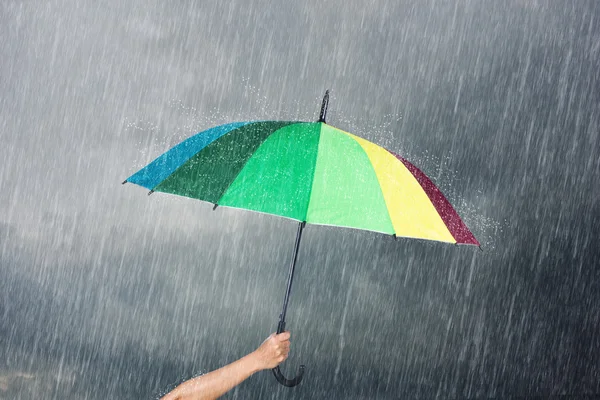 Mão segurando guarda-chuva multicolorido sob céu escuro com chuva — Fotografia de Stock