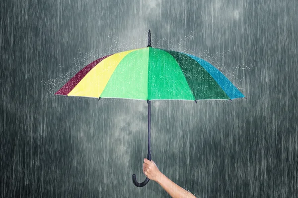 Mano sosteniendo paraguas multicolor bajo el cielo oscuro con lluvia — Foto de Stock