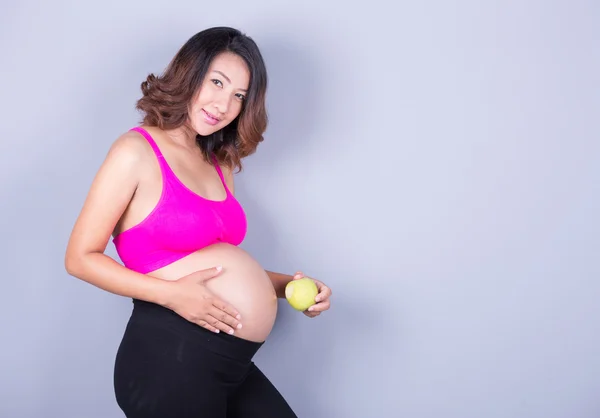 Mulher grávida bonita com maçã no fundo cinza — Fotografia de Stock