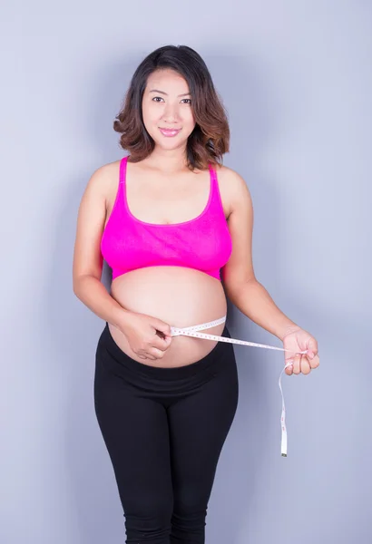 Mulher grávida com fita métrica em fundo cinza — Fotografia de Stock