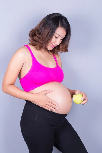 Mulher grávida bonita com maçã no fundo cinza — Fotografia de Stock