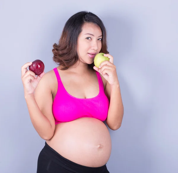Mulher grávida bonita com maçã no fundo cinza — Fotografia de Stock