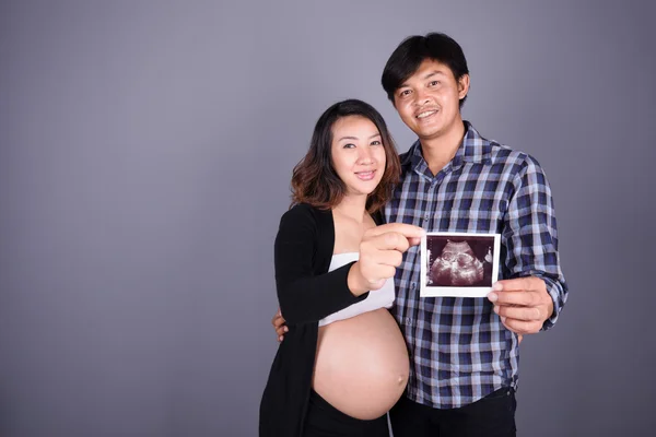 Felice incinta e marito che mostra l'immagine ecografica sulla schiena grigia — Foto Stock