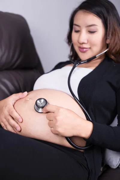 pregnant woman listening baby's heartbeat with stethoscope on he