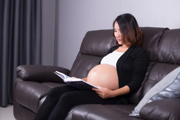 Mulher grávida deitada no sofá e livro de leitura — Fotografia de Stock