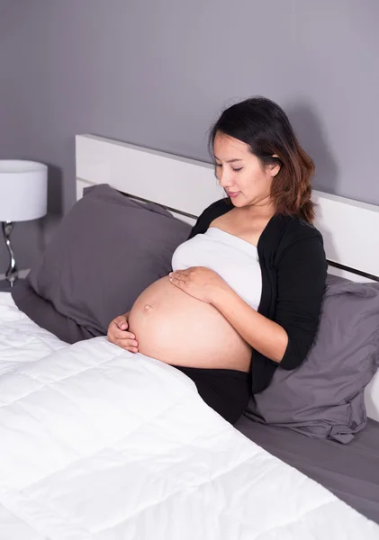Hamile kadın yatakta yatarken karnı arıyor — Stok fotoğraf