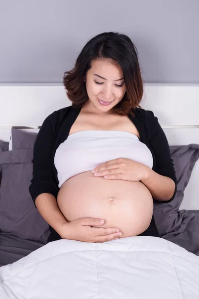 Mulher grávida olhando para a barriga enquanto deitada na cama — Fotografia de Stock