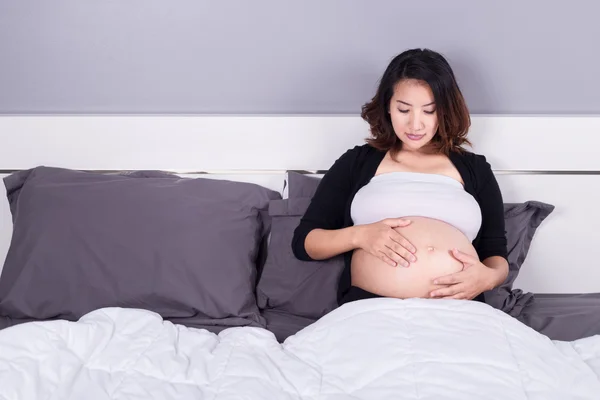 Hamile kadın yatakta yatarken karnı arıyor — Stok fotoğraf