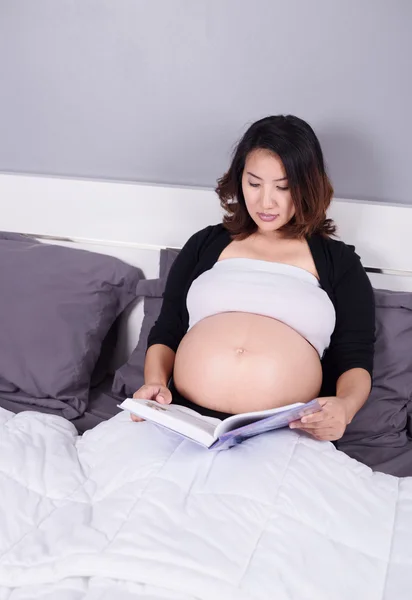Hamile kadın bedroo bir yatakta yatarken bir kitap okuma — Stok fotoğraf