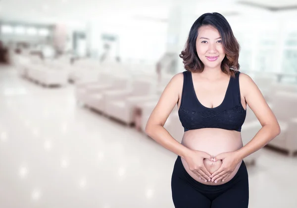 Mulher grávida segurando as mãos em forma de coração em sua barriga i — Fotografia de Stock