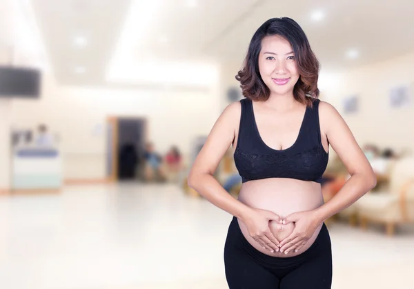 Mulher grávida segurando as mãos em forma de coração em sua barriga i — Fotografia de Stock