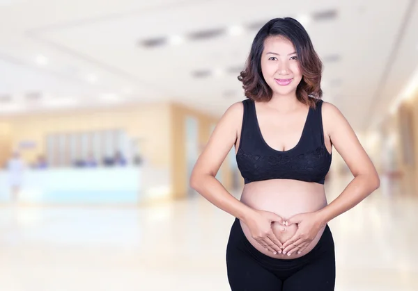 Mulher grávida segurando as mãos em forma de coração em sua barriga i — Fotografia de Stock