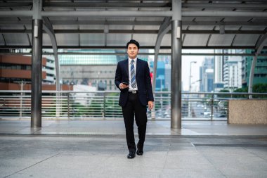 Takım elbiseli bir iş adamı şehirde yürüyor ve akıllı telefon kullanıyor.