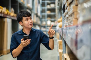 Depodaki envanteri kontrol etmek için akıllı telefon kullanan bir işçi.