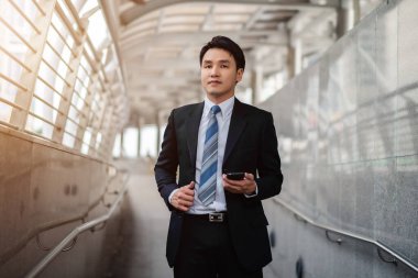 Takım elbiseli bir iş adamı şehirde yürüyor ve akıllı telefon kullanıyor.