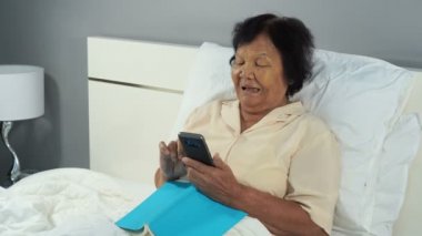 Yatakta cep telefonu kullanan son sınıf mutlu bir kadın.