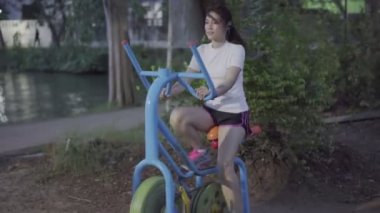 Parkta egzersiz bisikletinde çalışan bir kadın.