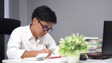 Genç adam dizüstü bilgisayarla ders çalışıyor ve yazıyor.