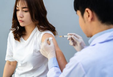 Doktorun elinde şırınga var ve hastaya iğne yapmadan önce pamuk kullanıyor. Covid-19 veya koronavirüs aşısı