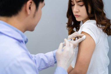 Doktorun elinde şırınga var ve hastaya iğne yapmadan önce pamuk kullanıyor. Covid-19 veya koronavirüs aşısı