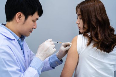 Doktorun elinde şırınga var ve hastaya iğne yapmadan önce pamuk kullanıyor. Covid-19 veya koronavirüs aşısı