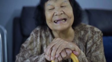 Oturma odasında yaşlı bir kadının gülüşü ve tahta bastonu ağır çekimde. 