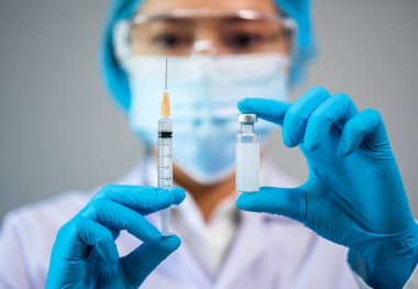 Kadın doktor elinde aşı şişesi ve şırınga ilacı tutuyor.