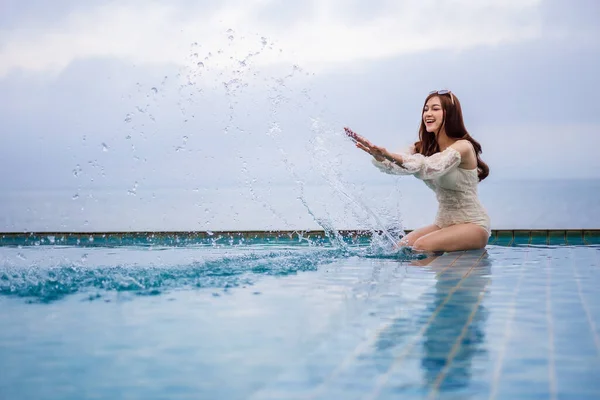 年轻女子在有大海背景的游泳池里玩水花 — 图库照片