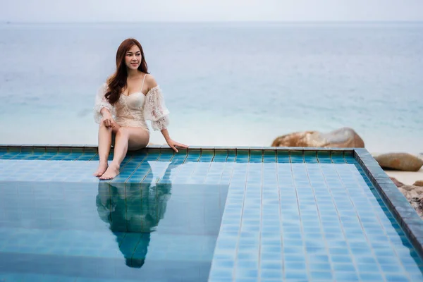 young woman sitting on edge of swimming pool and looking to the sea