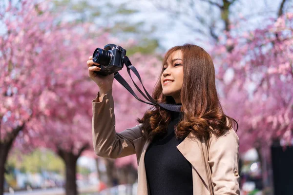 公園で写真を撮るために桜や桜の花を見てカメラを持っている若い女性旅行者 — ストック写真