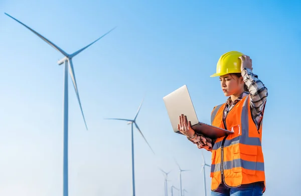 young stressed female engineer having problem to working with laptop computer against wind turbine farm