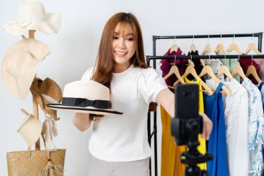 Genç bir kadın internette şapka ve giysi satıyor. Akıllı telefondan canlı yayın yapıyor. Evde internet üzerinden iş yapıyor.