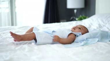 Küçük neşeli bebek, ellerini ve bacaklarını bir yatakta oynat.