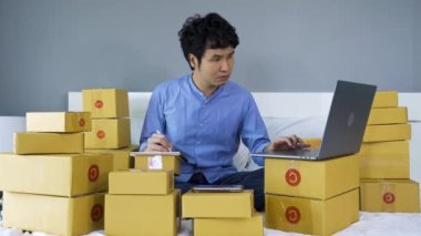 Stresli adam dizüstü bilgisayar kullanıyor ve evdeki bir yatakta online ürün satmak için çalışıyor.