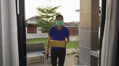 Teslimatçı kadın müşteriye paket teslim ederken, Coronavirus 'un yayılmasını önlemek için maske takmak zorundadır (Covid-19)