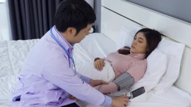 Doktor yatakta hasta bir kadının kan basıncını ölçüyor.