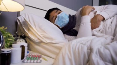 Tıbbi maskeli hasta adam virüs hastalığı ve yatakta ateş, koronavirüs (covid-19) pandemik konsept.