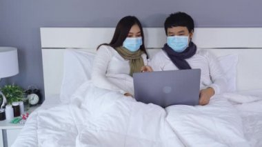 Karantina sırasında dizüstü bilgisayar kullanan tıbbi maskeli çift koronavirüs (covid-19) evde kalır..