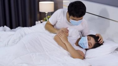 Adam hasta karısına evde bir yatakta bakıyor, Coronavirus 'u korumak için tıbbi maske takan çift (covid-19)