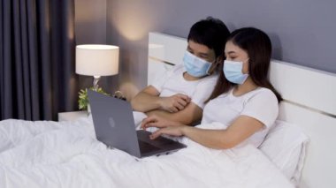 Karantina sırasında dizüstü bilgisayar kullanan tıbbi maskeli çift koronavirüs (covid-19) evde kalır..