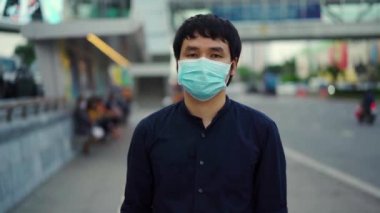 Yaya yolunda yürüyen ve Coronavirus (Covid-19) salgınını önlemek için tıbbi maske takan Asyalı genç bir adamın ağır çekimde şehir sokaklarında yürümesi. yeni normal kavramlar