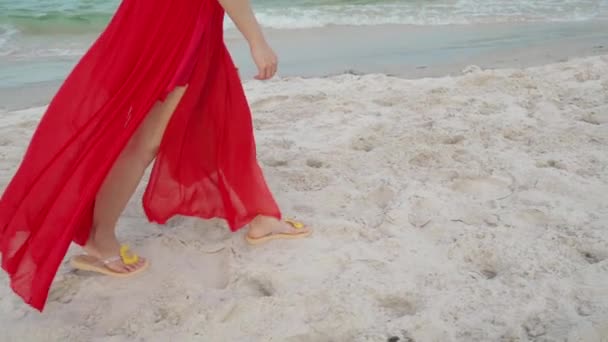 風の吹く海のビーチを歩く赤いドレスの女性の足の動き — ストック動画