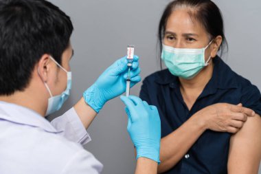 Doktor şırıngayı kadınlara enjekte etmeden ve maske takmadan önce şişeden ilaç alıyor. Covid-19 veya koronavirüs aşısı