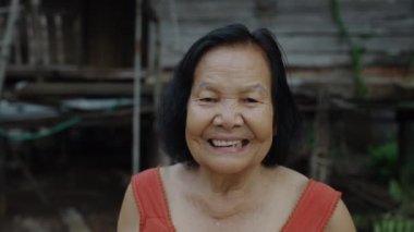 Yuvarlak boyunlu, kolsuz yakalı yaşlı bir kadın eski ahşap evde gülüyor.