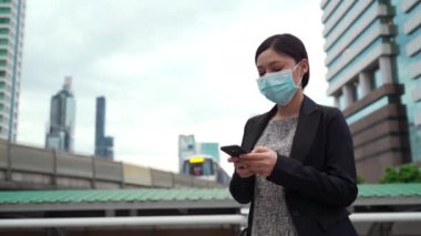 Şehirdeki Coronavirus (covid-19) salgınından korunmak için akıllı telefon kullanan ve tıbbi maske takan bir iş kadını