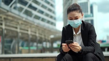 Şehirdeki Coronavirus (covid-19) salgınından korunmak için akıllı telefon kullanan ve tıbbi maske takan bir iş kadını
