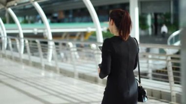 İş kadını şehirde yürüyor ve akıllı telefonunu kullanıyor.